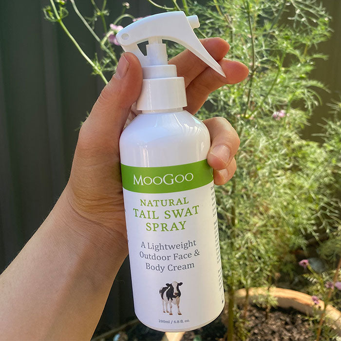 MooGoo Tail Swat Spray shown outdoors in hand, multipurpose natural spray to hydrate skin and provide outdoor protection against insects for all ages.