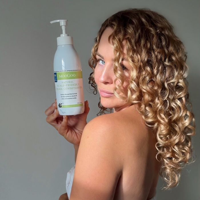MooGoo Natural Sensitive Scalp Cream Conditioner held by woman with long curly hair, natural silicone free conditioner for hydration and scalp health