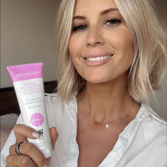 Close-up of MooGoo Protein Shot Leave-In Conditioner tube held by model, natural formula for stronger and healthier hair